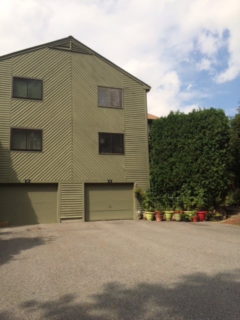A Ledgemere townhouse building with green siding, two garages and potted plants beside a tall hedge